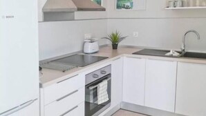 A modern kitchen with white cabinetry, a Bosch refrigerator, a built-in oven, a stovetop, and a sink. - DORAMAS APARTMENT, Tias (Puerto del Carmen, Tias)