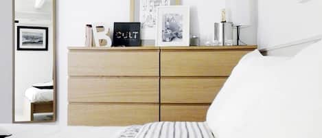 A bedroom with a bed, a wooden dresser, a mirror, and framed pictures on the wall.