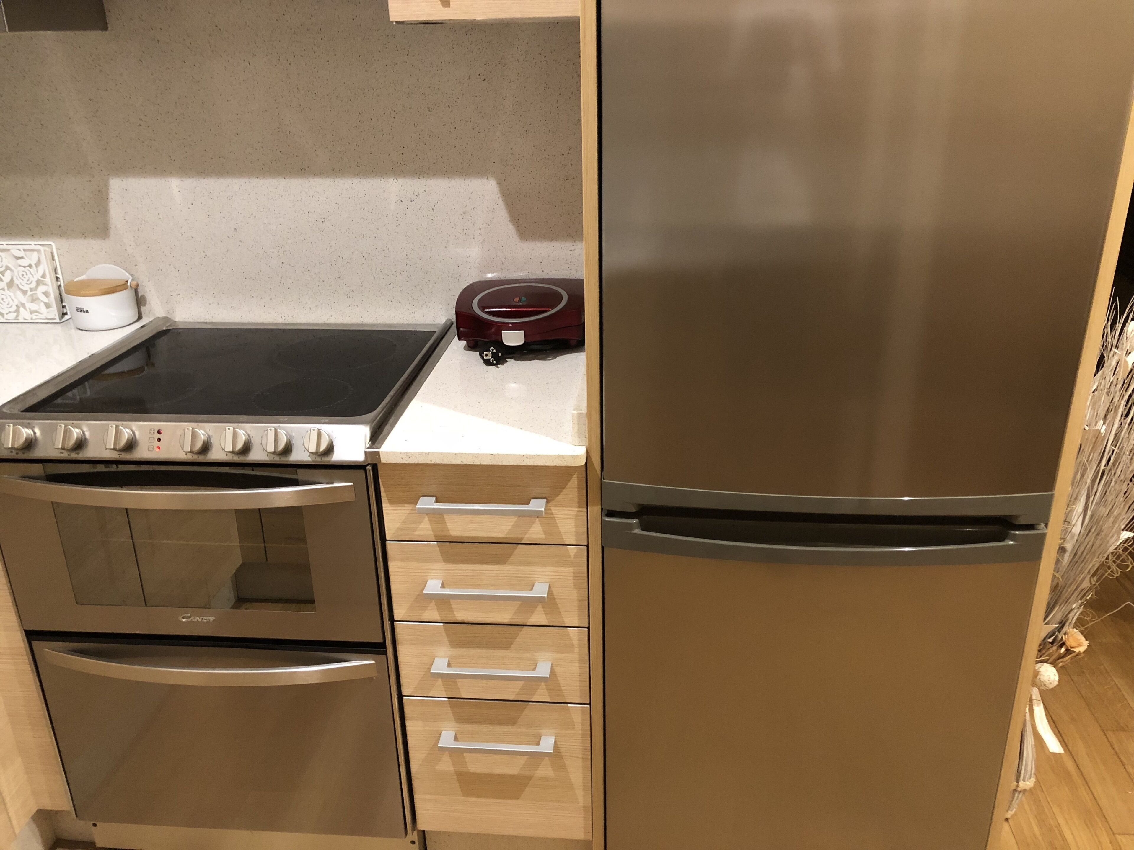 Une cuisine équipée d’une cuisinière, d’un four et d’un réfrigérateur en acier inoxydable, de meubles de rangement en bois et d’un plan de travail sur lequel se trouvent une machine à café et un appareil de couleur rouge.