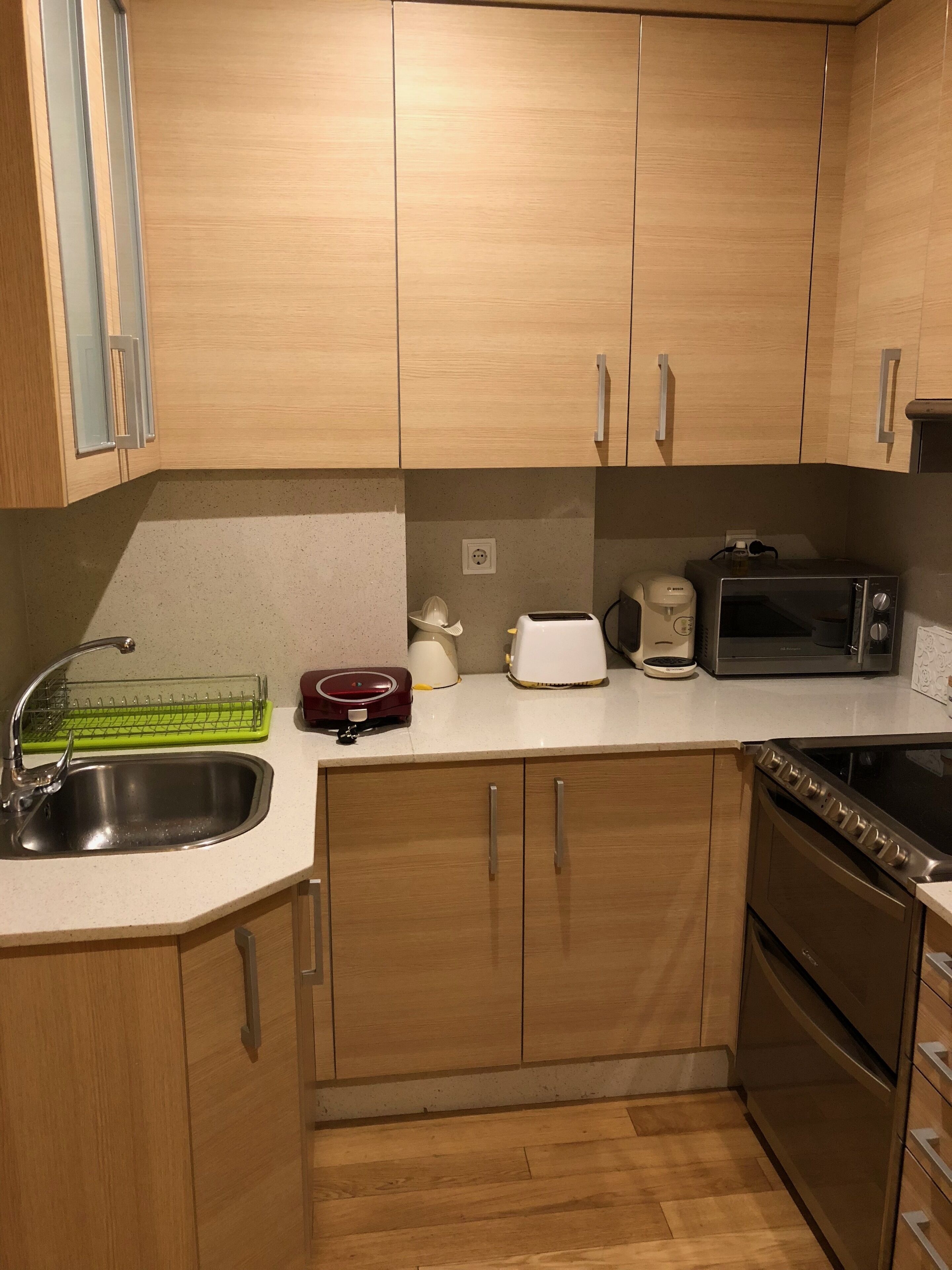 Una cocina con armarios de madera, un lavamanos de acero inoxidable, un microondas, un tostador y un electrodoméstico rojo sobre la encimera.