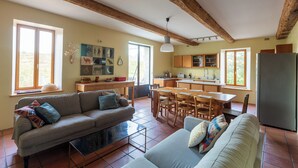 Een ruime woonkamer met een bank, een eettafel en een keuken op de achtergrond.