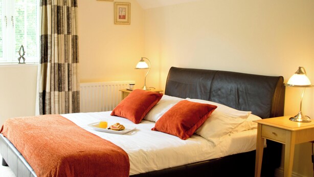 Een slaapkamer met een bed, een bureau, een stoel, een raam met gordijnen en een radiator.