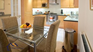 Een moderne keuken met houten kastjes, een roestvrijstalen spoelbak en een glazen eettafel met stoelen.
