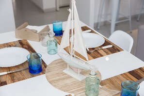 Una mesa de comedor con un barco modelo, vasos azules y un mantel individual de madera.