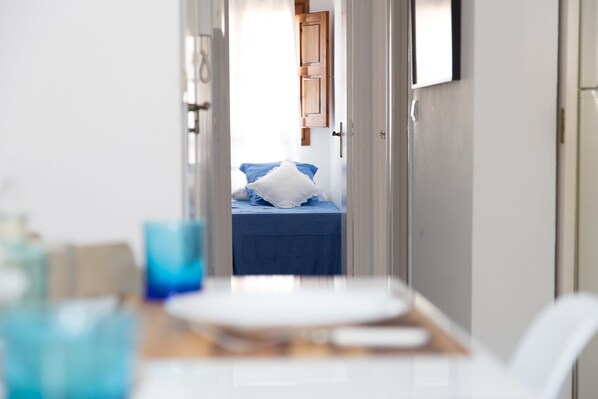 Un pasillo estrecho que conduce a una habitación con una cama, una mesita y una silla.