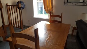 Une table à manger en bois avec des chaises, une fenêtre avec des rideaux, un radiateur et une petite table avec une lampe.