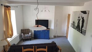 Un salon avec un canapé, un fauteuil, un téléviseur, un porte-manteau et un tableau accroché au mur.