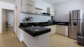 A modern kitchen with white cabinets, a black countertop, a stainless steel refrigerator, and a potted plant.