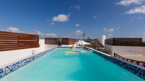 A swimming pool with a blue mosaic border, surrounded by wooden fences, and a clear sky above.