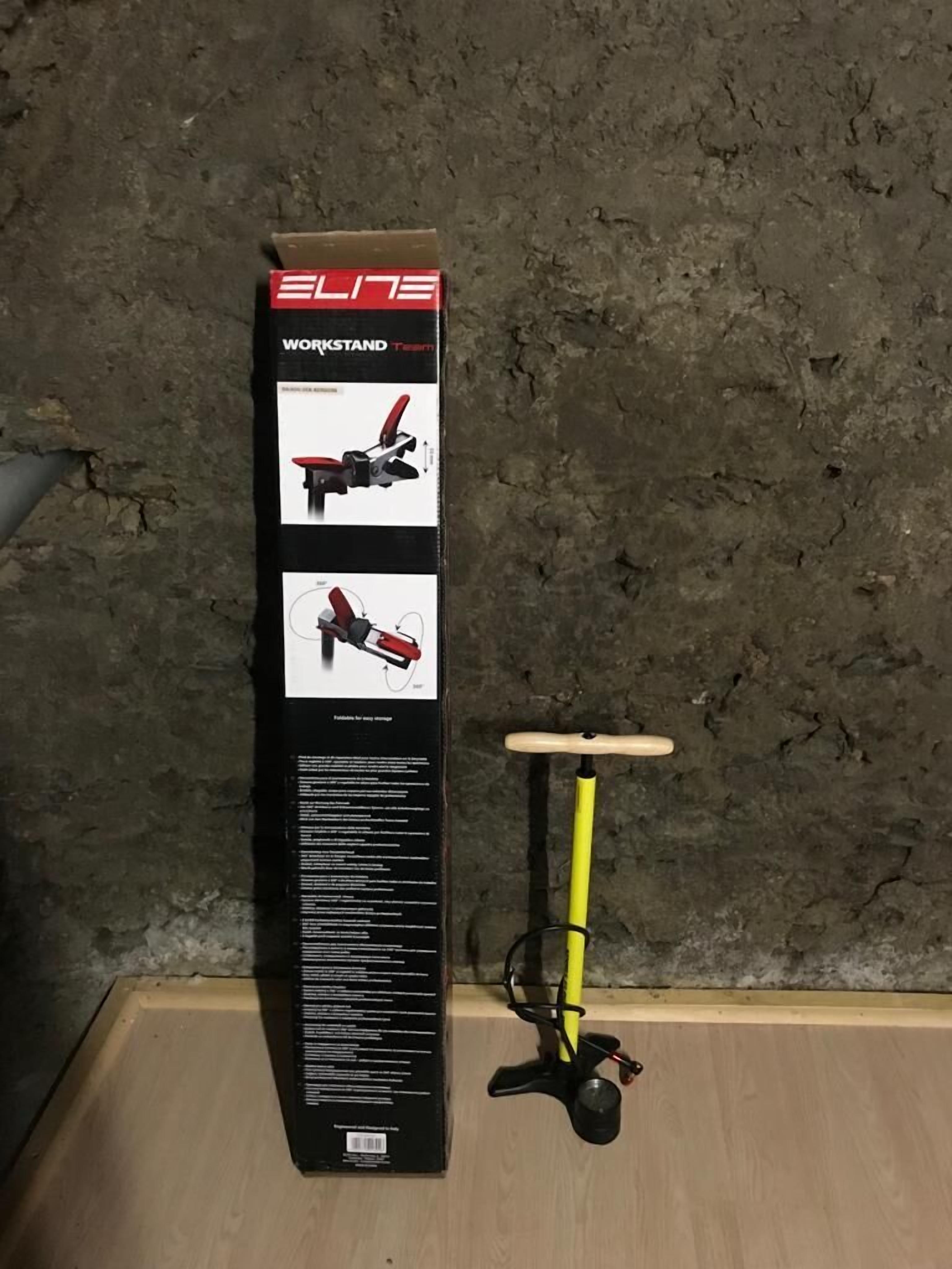 A workstand with a yellow pole and black base, placed against a textured wall.