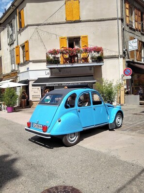 Un coche azul antiguo estacionado frente a un edificio con un letrero que dice 'Le Bijou d'Art'.