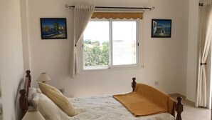 A bedroom with a bed, a ceiling fan, a window with curtains, and two paintings on the walls. - Spacious,quiet villa in a secluded tranquil location with all amenities nearby (Peyia)