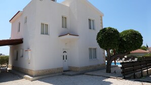 A white building with a flat roof, a door, and windows. There is a tree and a bench in the foreground. - Spacious,quiet villa in a secluded tranquil location with all amenities nearby (Peyia)