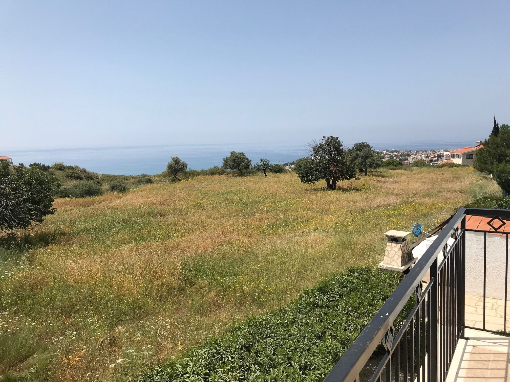A balcony with a view of a grassy field, trees, and a distant coastline.