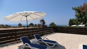 A terrace with two lounge chairs and a large umbrella, overlooking a scenic view of the sea and hills. - Spacious,quiet villa in a secluded tranquil location with all amenities nearby (Peyia)
