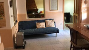 A living room with a sofa, a dining table, and a kitchen area in the background. - Anna Apartment- Villaputzu center Apartment (Villaputzu)