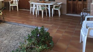 A patio with a round table and chairs, a potted plant, and a wooden door. - Anna Apartment- Villaputzu center Apartment (Villaputzu)