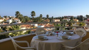 Comedor con una mesa dispuesta para cuatro personas, con vista a una zona residencial con palmeras y casas.