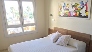 Un dormitorio con una cama, almohadas, una mesita de noche y un cuadro en la pared.