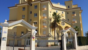 Un edificio de varios pisos con fachada amarilla, balcones y una entrada protegida por una reja.