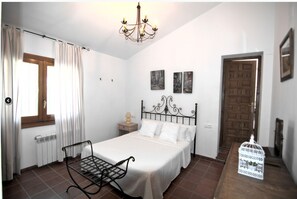 A bedroom with a bed, a radiator, a window with curtains, a chandelier, and a door.