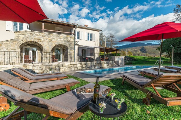 A poolside area with lounge chairs, a table with a bottle and glasses, and a stone building with a pool. - Village stone Villa Ana Boljun (Boljun)