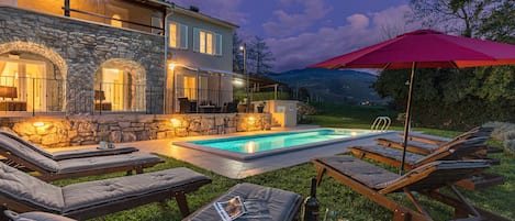 Un espace aménagé au bord de la piscine, avec des chaises longues, un mur en pierre et une piscine.