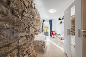 A room with a stone wall, a bed with a floral bedspread, a small table with a chair, and a red chair. - Village stone Villa Ana Boljun (Boljun)