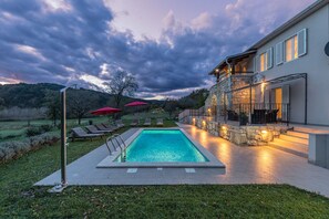 A swimming pool with lounge chairs and umbrellas, a stone building with a balcony, and a mountainous backdrop. - Village stone Villa Ana Boljun (Boljun)