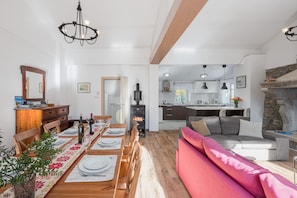 Tilava olohuone, jossa on kuuden hengen ruokapöytä, punainen sohva ja taustalla keittiö.