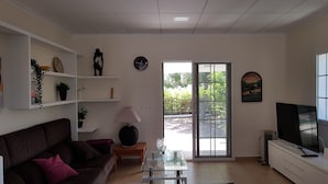 A living room with a sofa, a glass coffee table, a lamp, a TV, and a sliding glass door leading to a garden. - Excelent house in front of Golf filds / privat pool (Alicante)