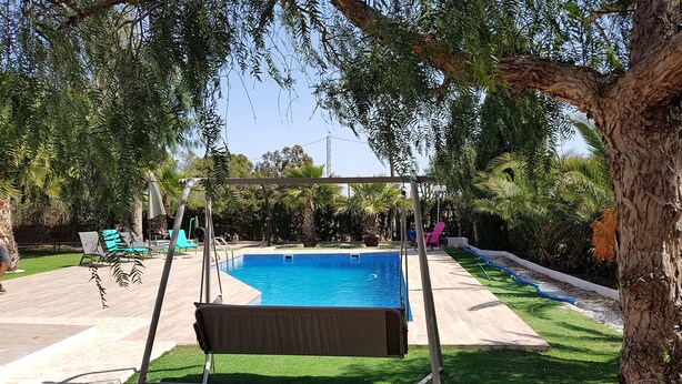 A backyard with a swimming pool, a swing set, and a patio area with chairs and tables. - Excelent house in front of Golf filds / privat pool (Alicante)