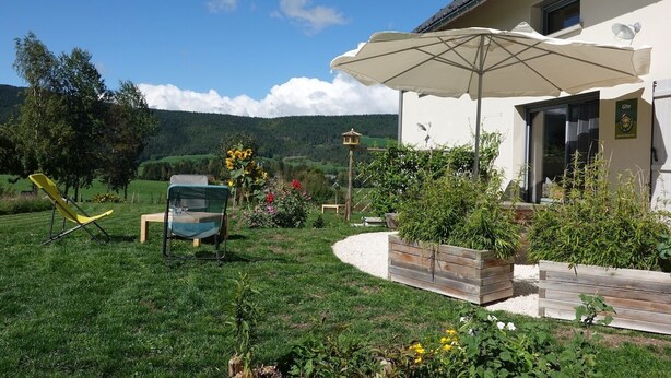 A garden with a wooden deck, a yellow chair, and a large umbrella. - Facing south, garden, exceptional view, super equipped. Ideal for 2 families (Lans-en-Vercors)