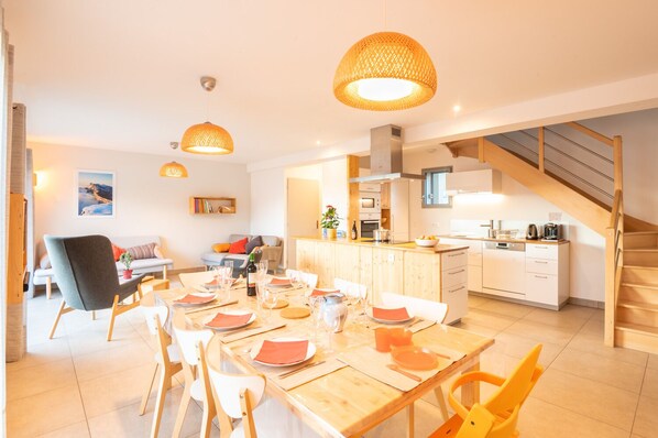 A modern kitchen with wooden cabinets, a dining area with a wooden table set for six, and a staircase leading to an upper level.