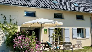 A building with a sloped roof, a covered outdoor seating area with a table and chairs, and a sign indicating a location. - Facing south, garden, exceptional view, super equipped. Ideal for 2 families (Lans-en-Vercors)