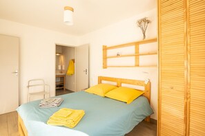 A bedroom with a bed, a wooden wardrobe, a shelf with dried flowers, and a chair.