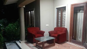 An outdoor seating area with two red chairs and a glass-top table, a tiled patio, and a door with a metal grill. - 150 Kalhaar Blues Greens- Golfers retreat. (Vasna Iyava)