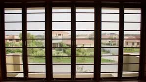 A view through a window with multiple panes, revealing a residential area with houses and greenery. - 150 Kalhaar Blues Greens- Golfers retreat. (Vasna Iyava)