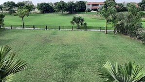 A well-maintained grassy area with a fence, palm trees, and a building in the background. - 150 Kalhaar Blues Greens- Golfers retreat. (Vasna Iyava)