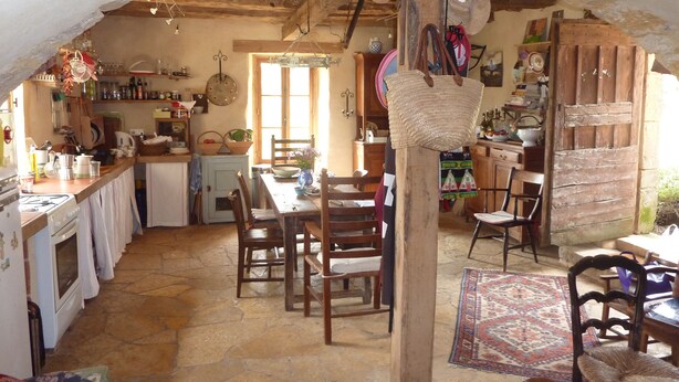 Une cuisine rustique avec un sol en pierre, des meubles en bois et un panier suspendu.