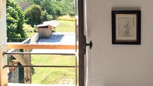 Une pièce avec une fenêtre donnant sur un paysage verdoyant, un tableau encadré accroché au mur et un radiateur placé sous la fenêtre.