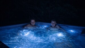 Two individuals in a hot tub with water jets, surrounded by darkness and foliage. - Unique vacation home with a hot tub in nature (Meeuwen-Gruitrode)