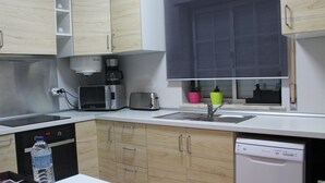 A modern kitchen with wooden cabinets, a built-in dishwasher, a coffee maker, and a window with a view. - Lara Apartment (Albufeira)