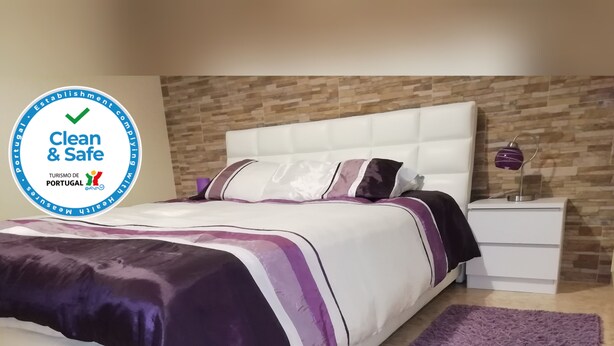 A bedroom with a bed, nightstand, and a purple rug. - Lara Apartment (Albufeira)