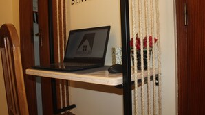 A laptop on a wooden shelf with a mouse, a sign reading "BENVENUTO", and a rope curtain with red flowers. - Lara Apartment (Albufeira)