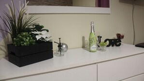 A white counter with a black planter box containing green plants and white flowers. A bottle of champagne and a glass are on the counter. - Lara Apartment (Albufeira)