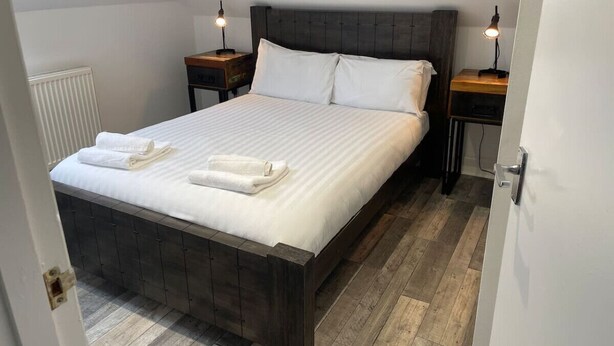 A neatly made bed with white linens and two towels, a dark wooden headboard, and two bedside tables with lamps. - Elder Park Apartment 5 The Loft (Glasgow)