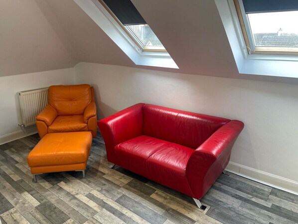 A room with a red leather sofa, an orange leather armchair, and a wooden parquet floor. - Elder Park Apartment 5 The Loft (Glasgow)
