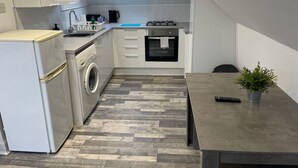 A compact kitchen with a washing machine, a stove, and a small dining area with a plant. - Elder Park Apartment 5 The Loft (Glasgow)