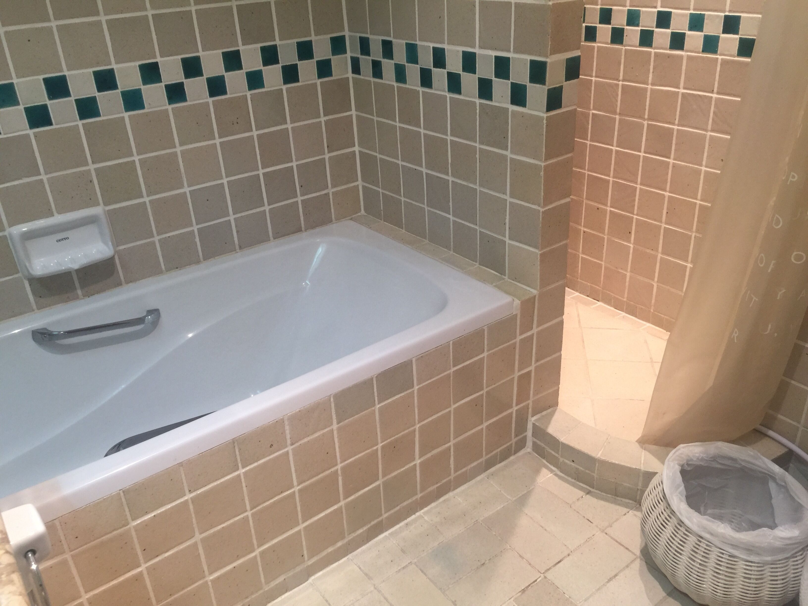 A bathroom with a bathtub, tiled walls, a handrail, and a trash bin.